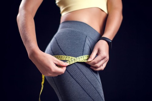 Woman with short blond hair in sport clothes measusing her buttock. Fitness and healthcare concept