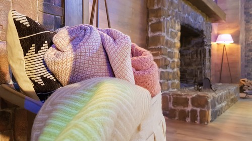 Knitted and warm blankets are folded and laid in a wicker basket near the fireplace. Cozy interior in the house. Details of a modern cozy interior