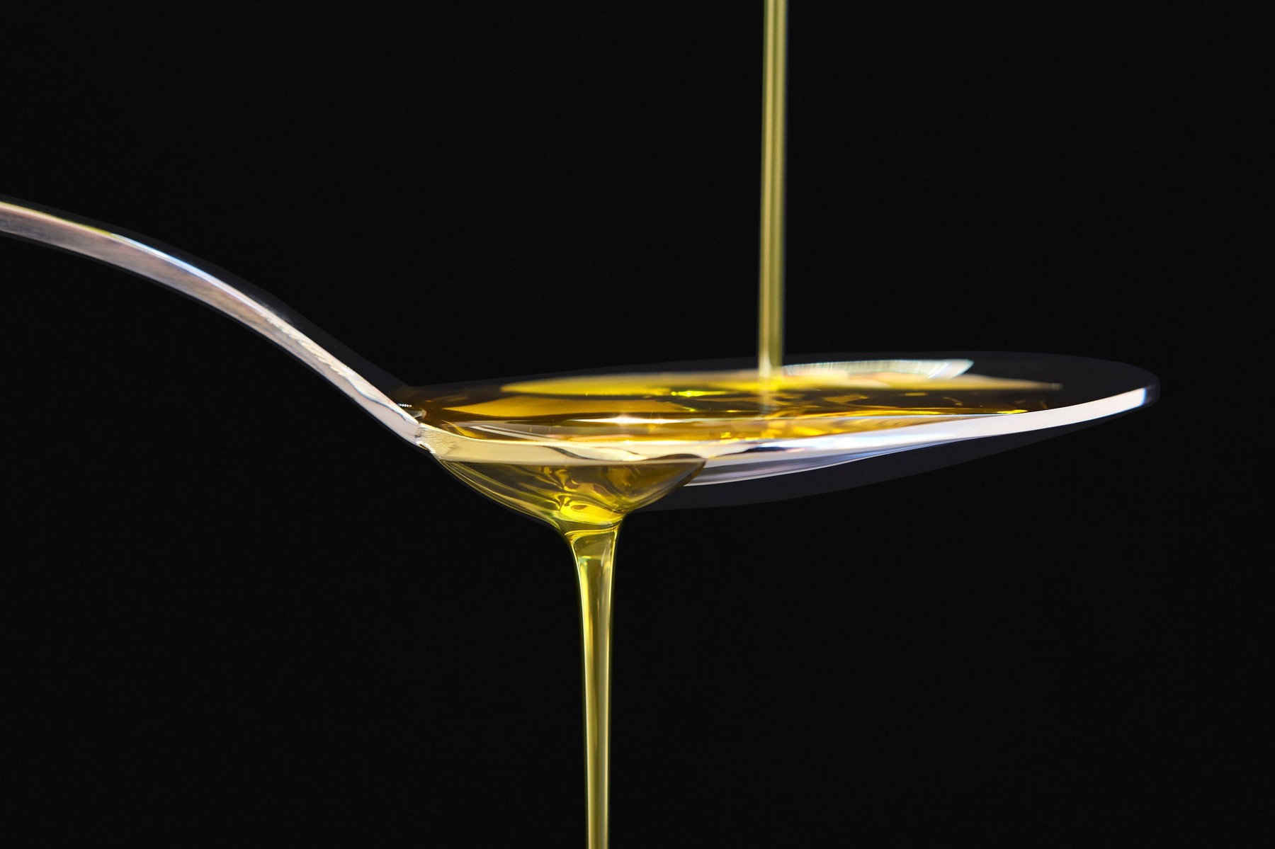 Olive oil liquid on a spoon over black background. Cooking