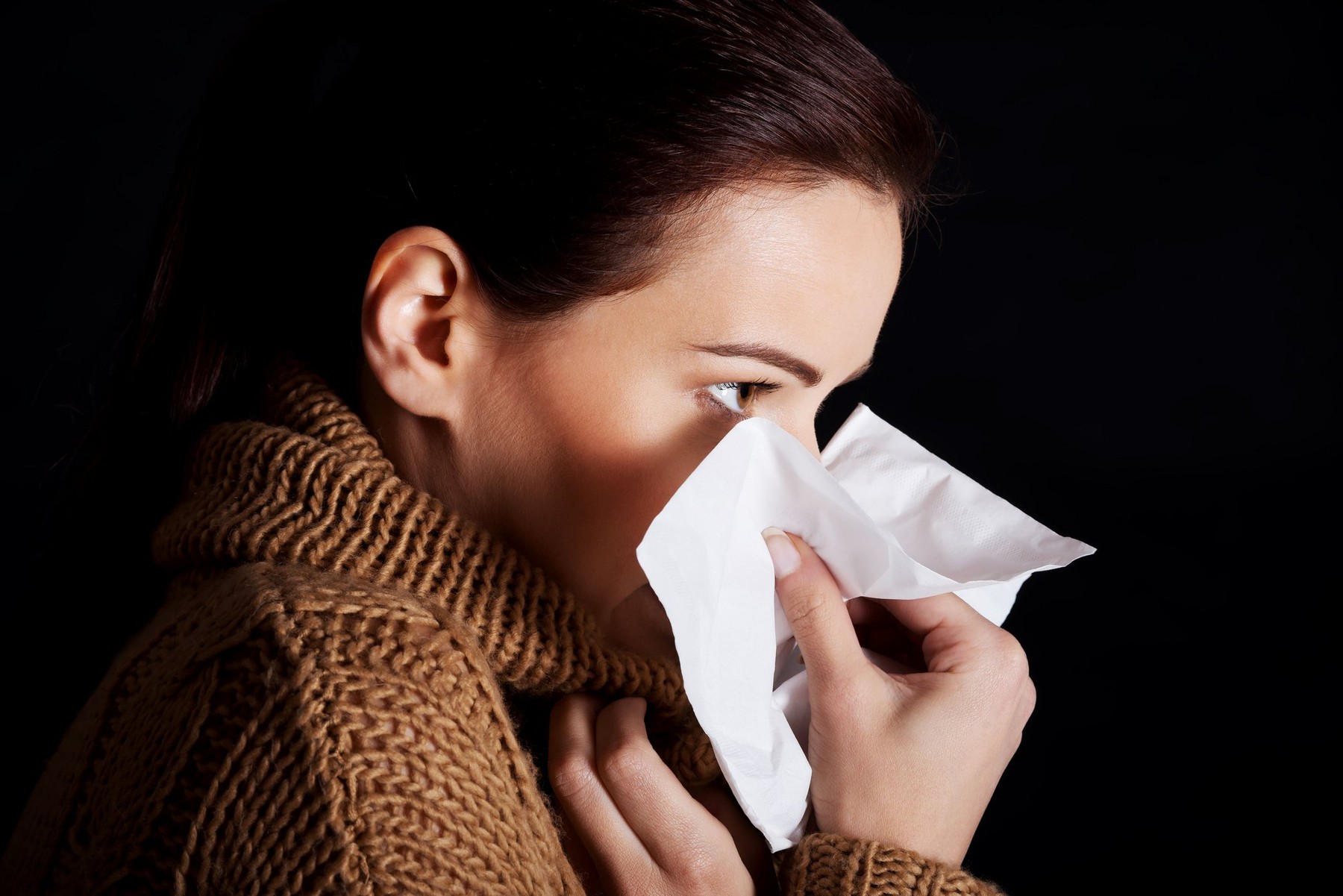 Sad young girl with tissue. Over black background.