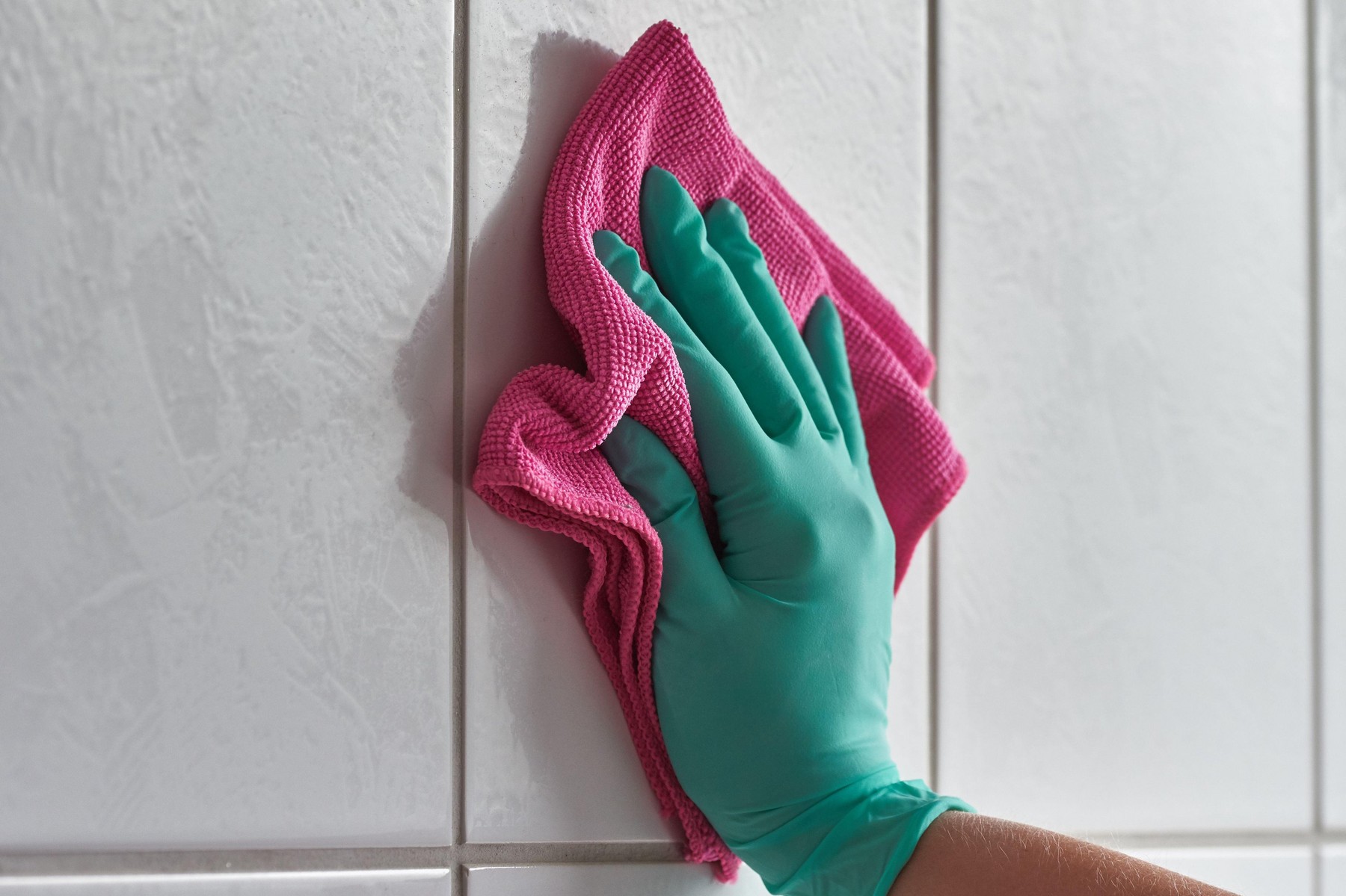 Close-up of female hand with glove and microfiber cloth cleaning white bathroom tiles