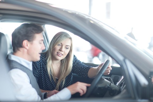 Car salesman advising young woman in car showroom