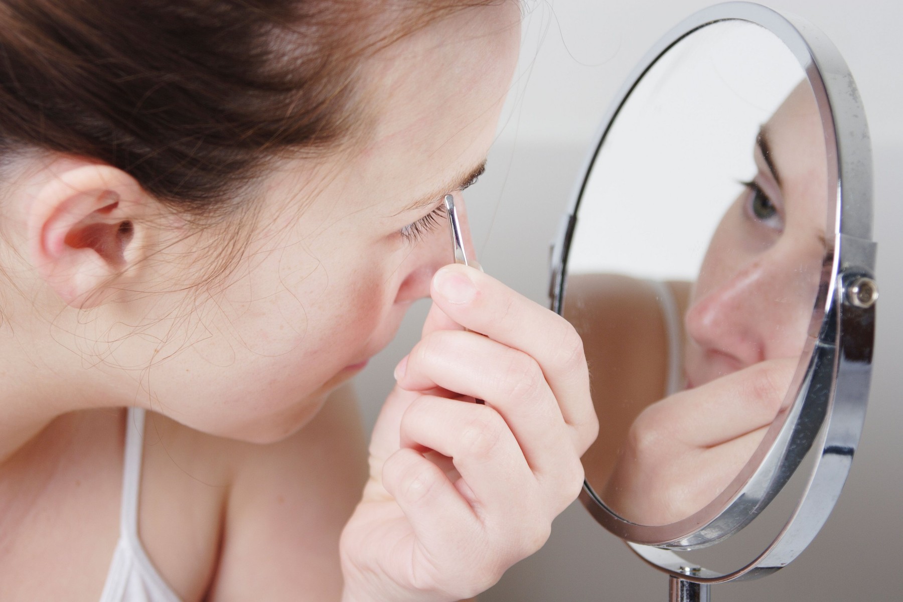 woman plucking eyebrows in mirror