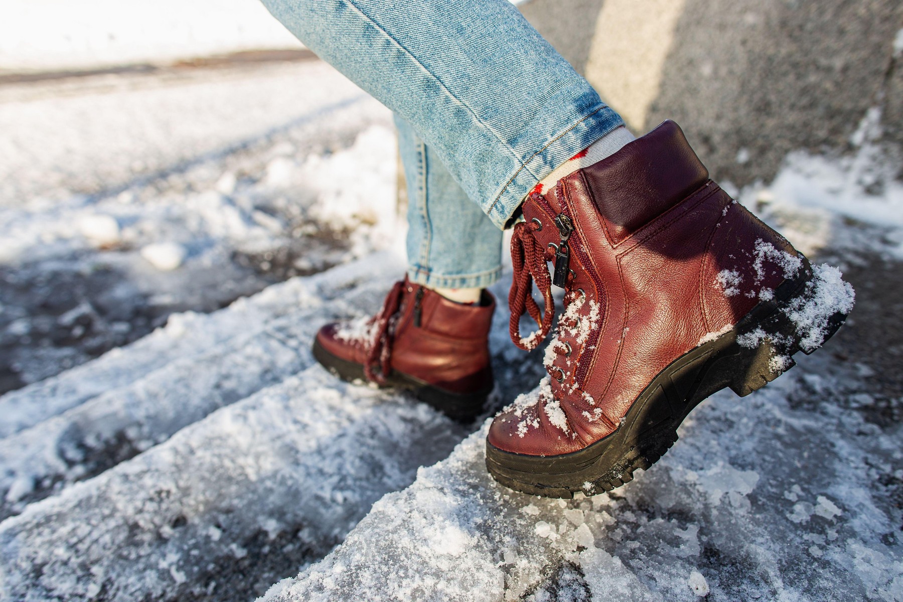 Winter is coming. Female boots on rough slipper ice surface. A woman in vinous leather shoes descends the slippery ice ladder.