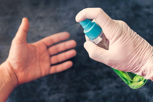 Cleaning of hands from bacteria and microbes with alcohol spray, prevention of coronavirus and other diseases. A gloved hand sprays aerosol on a clean