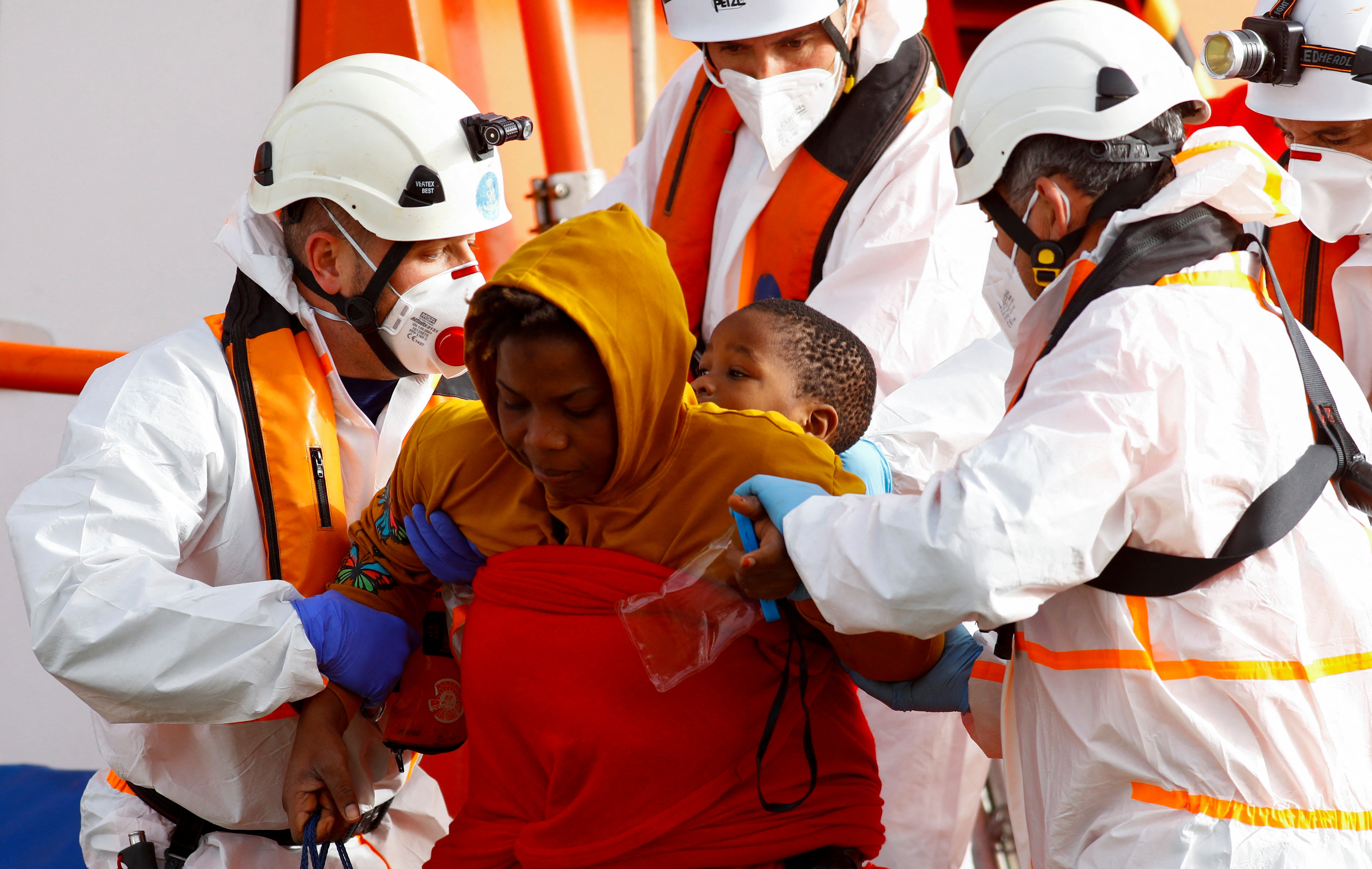 Rescuers help a migrant and her baby to disembark from a Spanish Coast Guard vessel, in the port of Arguineguin