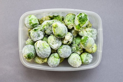 Frozen brussels sprouts in a plastic container for long-term storage. Deep freezing of vegetables. Frozen food vegetables on grey background.
