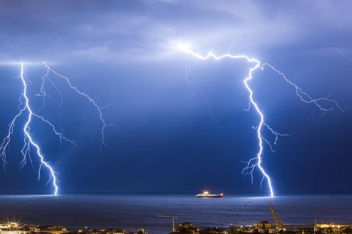 Massive cloud to ground lightning bolts hitting the horizon of city lights