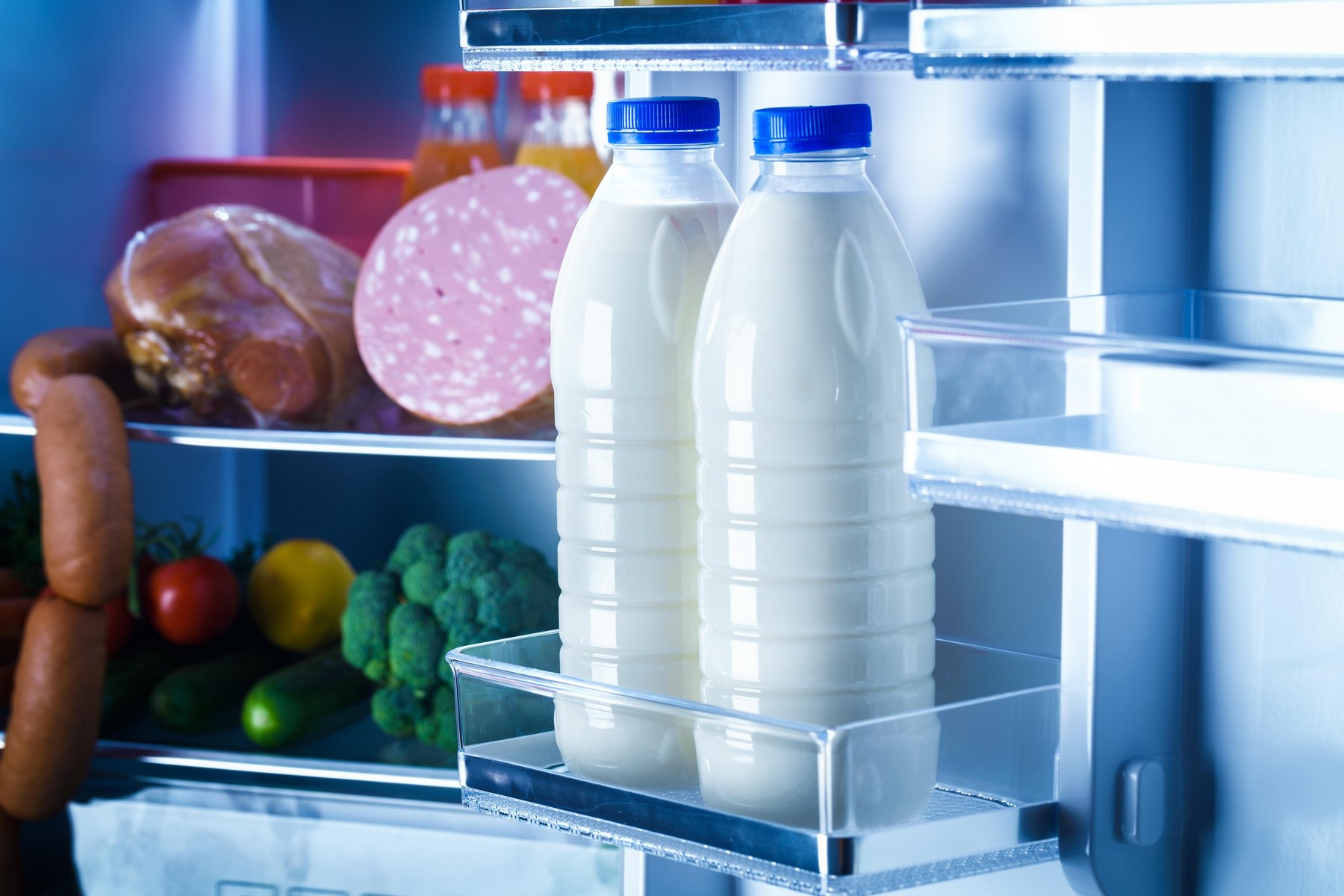Open refrigerator filled with food. Focus on Bottles of milk in the fridge