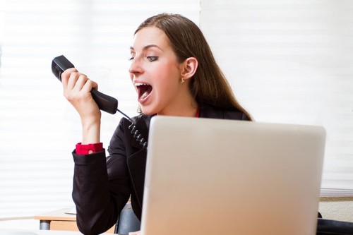 A young executive woman shouts to the phone at the office