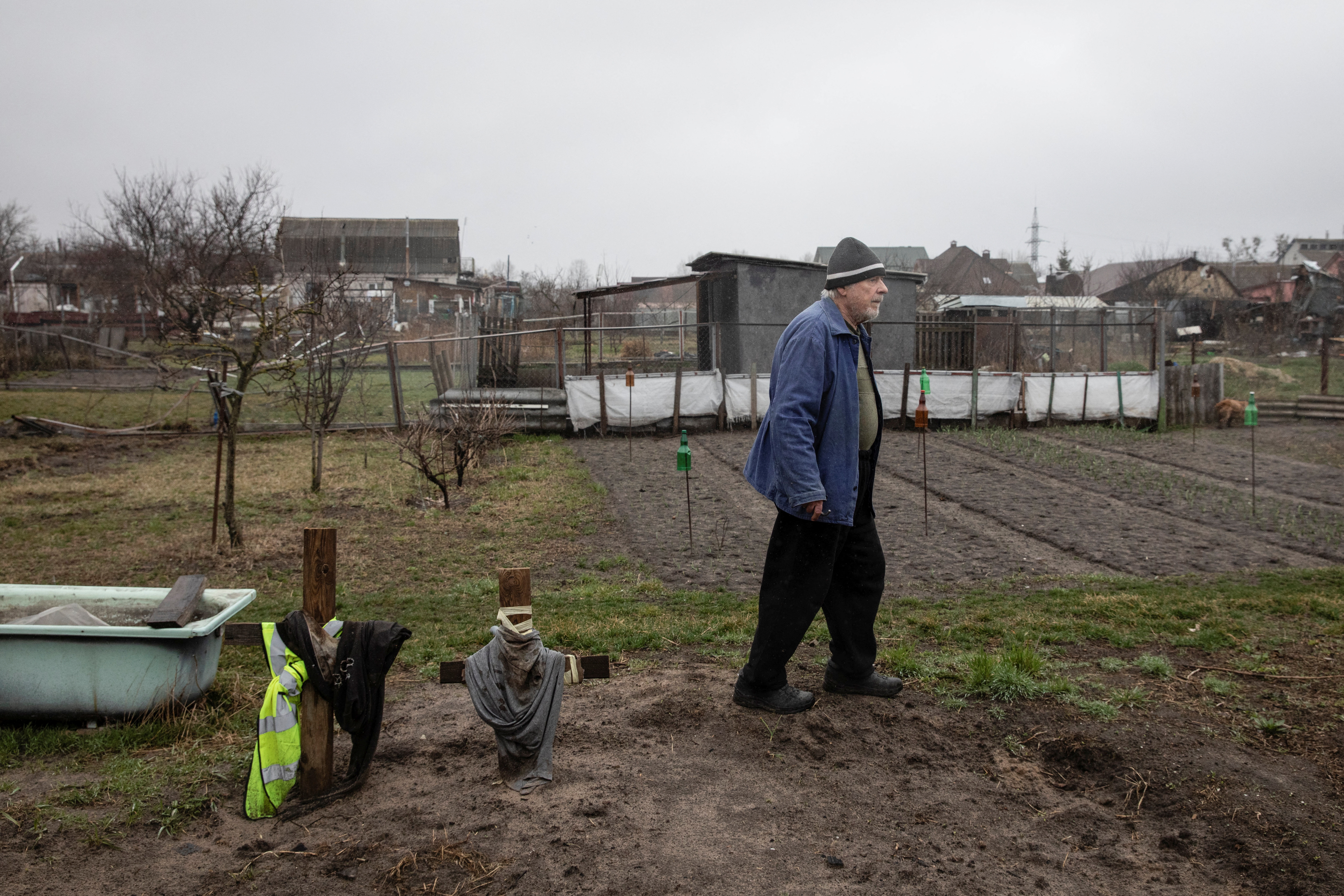 A man stands next to graves of people whom he buried at a backyard of his house in the settlement of Hostomel