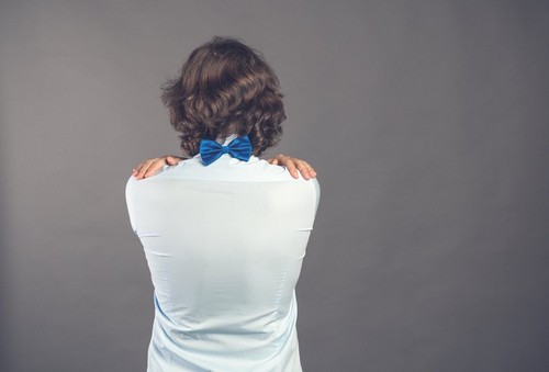Young man in blue shirt and bow tie hugs himself on grey background. Rear view. His hands lie on the back. He needs to be embraced. Selfish feeling, love yourself concept. Positive emotion. Copy space