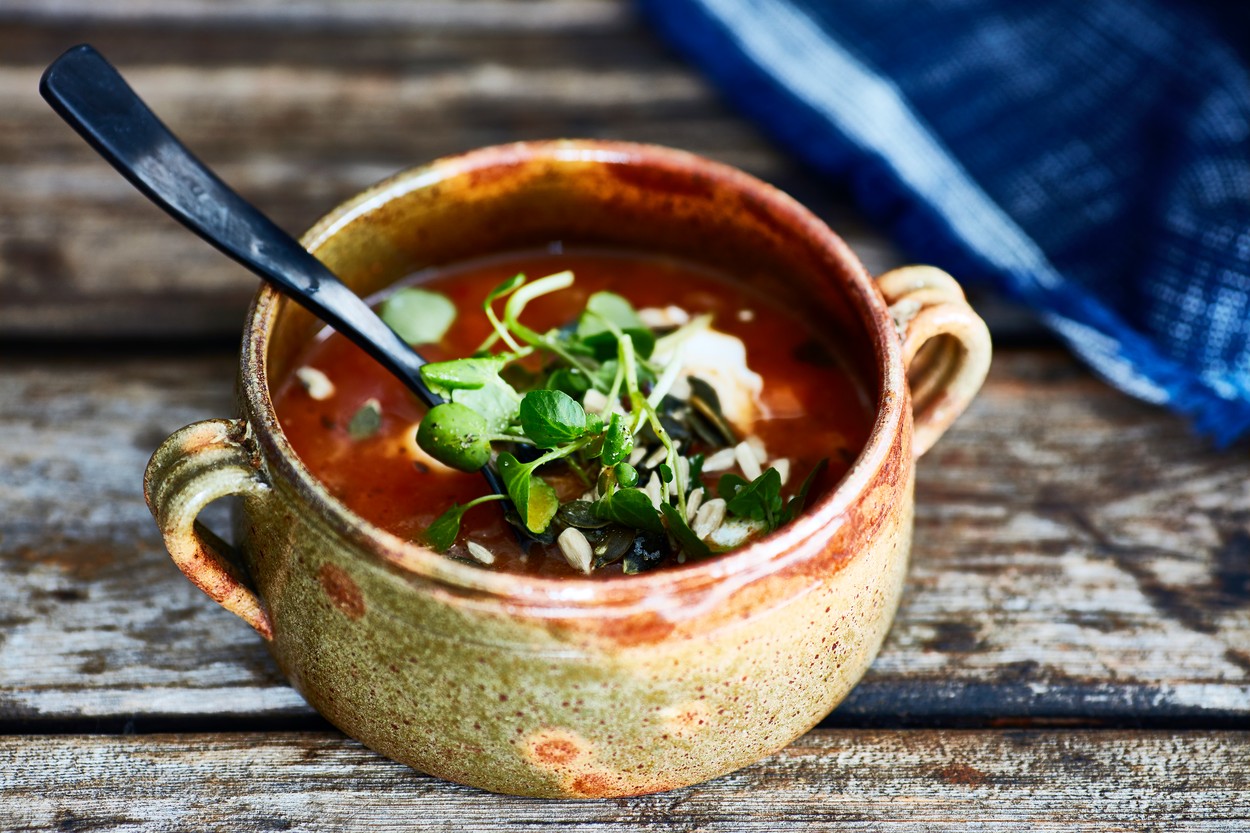 Bowl of soup garnished with watercress, on wooden table