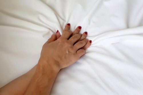 Couple having sex, male and female hands with red nails pulling and gripping white bedsheet in ecstasy. Orgasm of woman on the bed, concept of passion