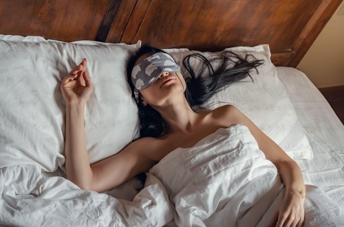 Woman sleeping in a sleep mask in bed with white sheets on vintage bed