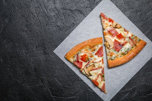 Cut into slices delicious fresh pizza with mushrooms and ham on a dark background. Top view . Pizza on the black table.