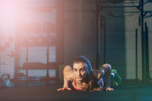 Fit woman in colourful sportswear doing burpees on a exercise mat in a grungy industrial type space