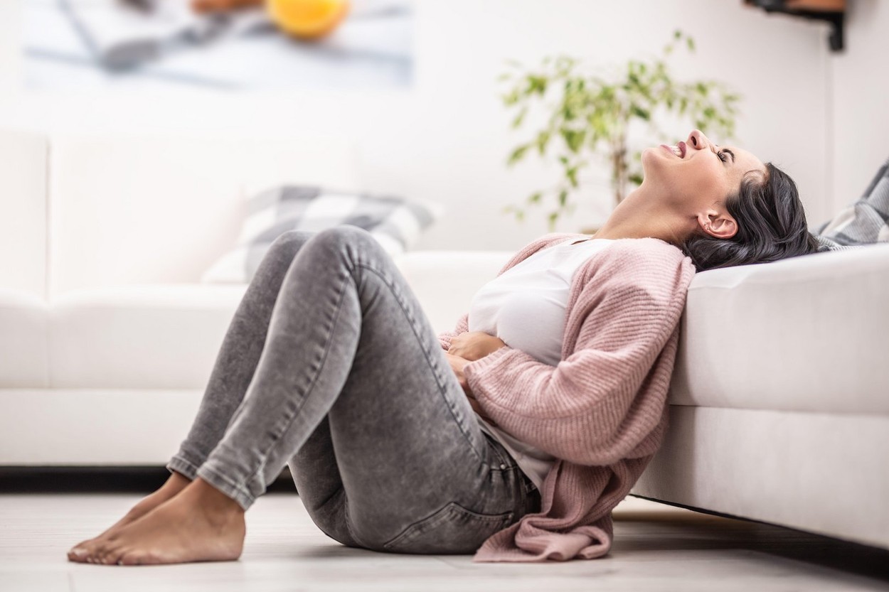 Intense menstruation pain freezes a woman sitting on the floor at home.