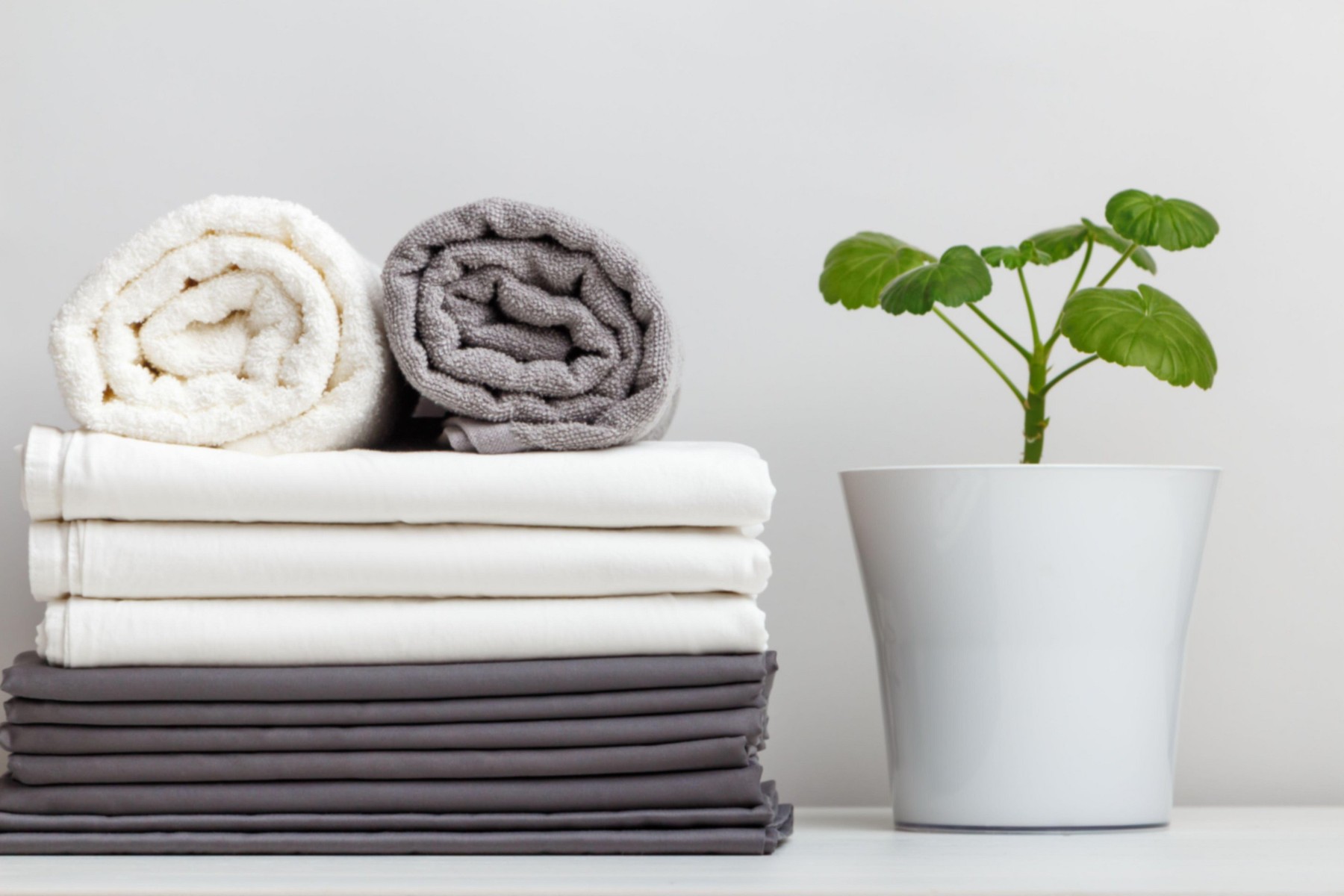 A stack of gray and white linens, sheets and towels on the table. Plant in the pot
