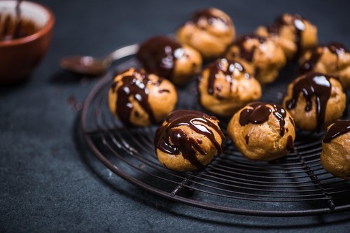 profiteroles eclairs resting on cooling rack, topped with melted dark chocolate