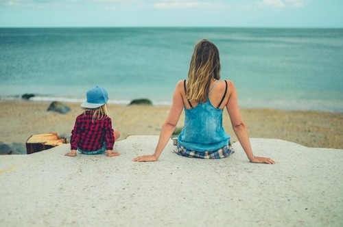 A young mother and her toddler are sitting on a concrete pier by the sea