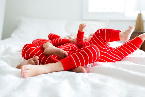 Siblings (2-3, 4-5) in red pajamas lying on bed