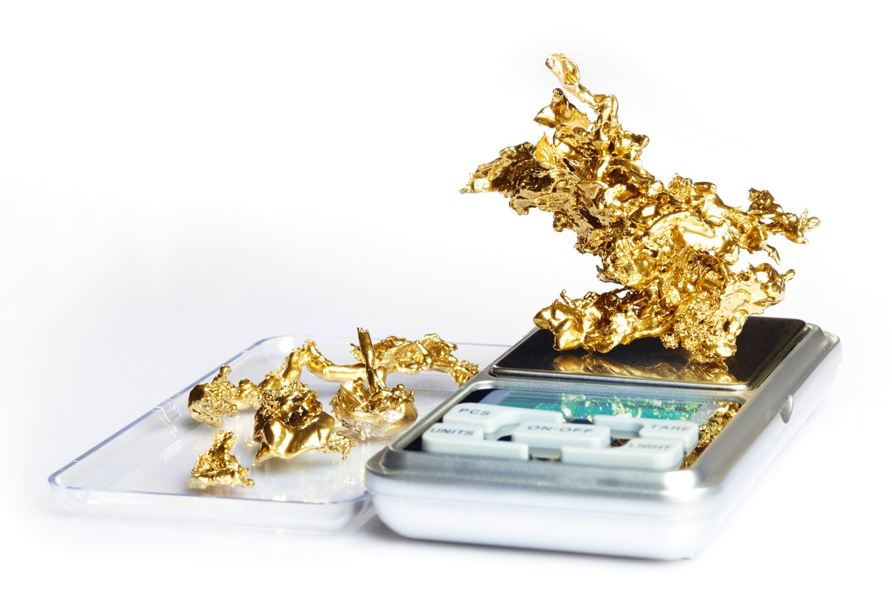 Beautiful pieces of raw gold ore weighted on digital scale on white background