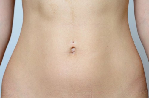 Flat Belly of a Bare Young Slender Woman in Close up Against Gray Background.