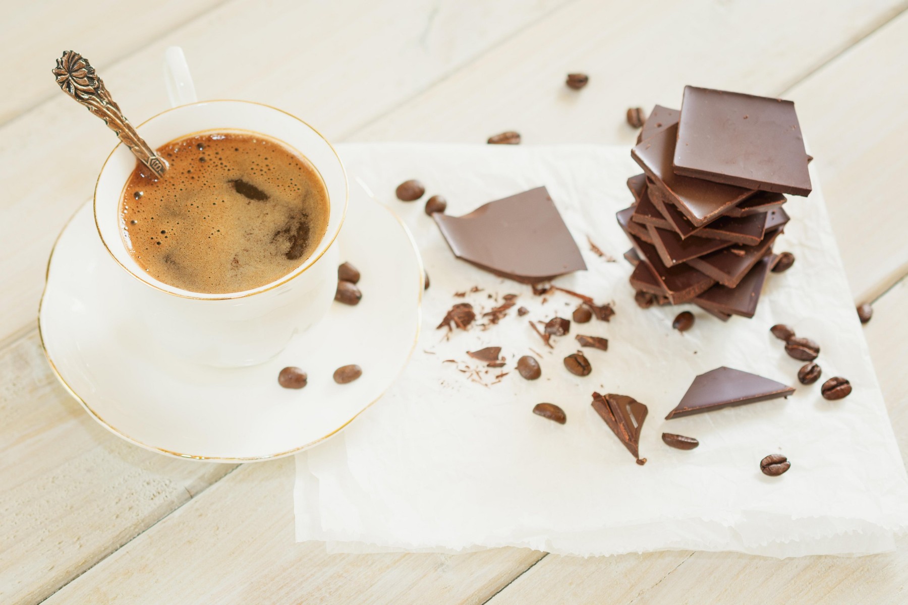 Pieces of chocolate with a cup of coffe presented on a white napkin decorated with loose coffee beans