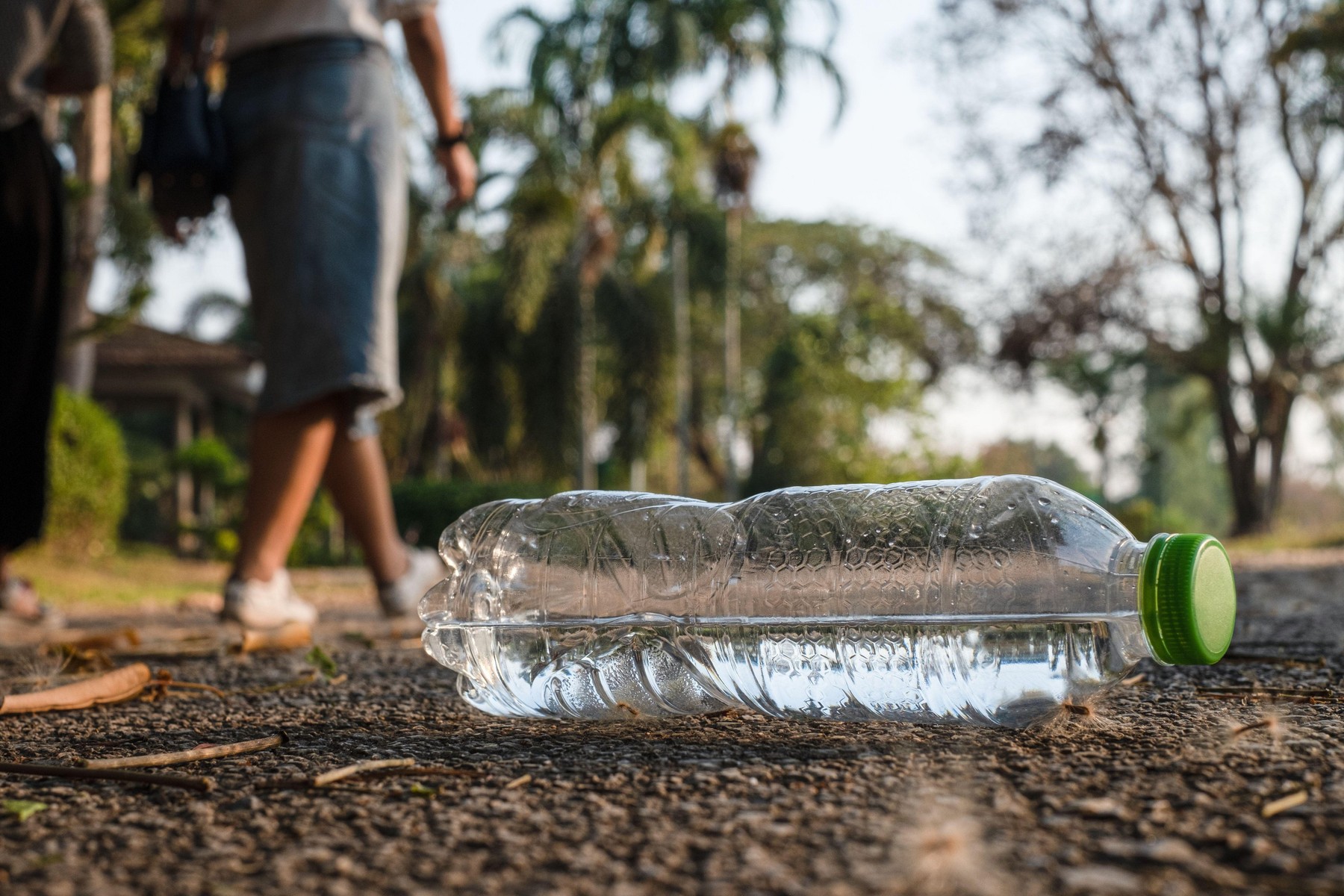 Close up clear plastic bottle water drink with a green cap on the road in the park at blurred background, Trash that is left outside the bin, litter o