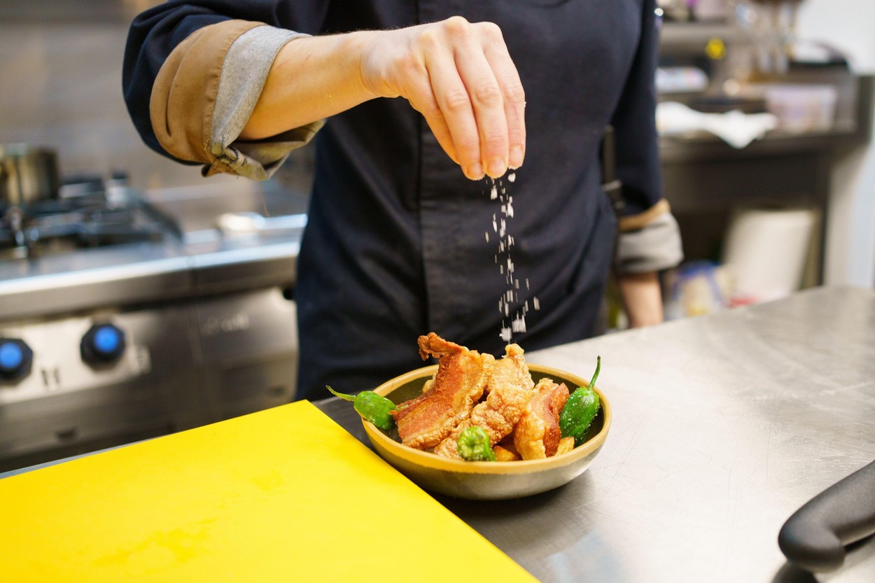 Crop chef garnishing a dish of pork and hot peppers in restaurant