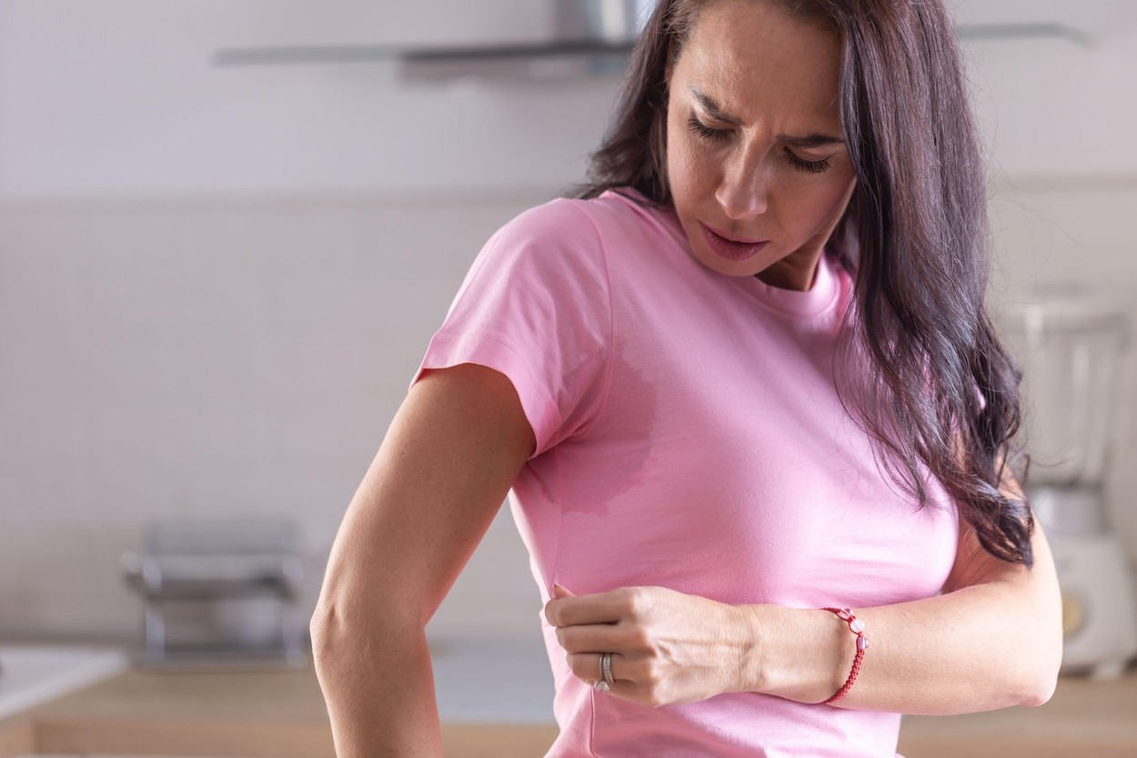 Excessive sweating visible by stains on a pink shirt of a young woman.