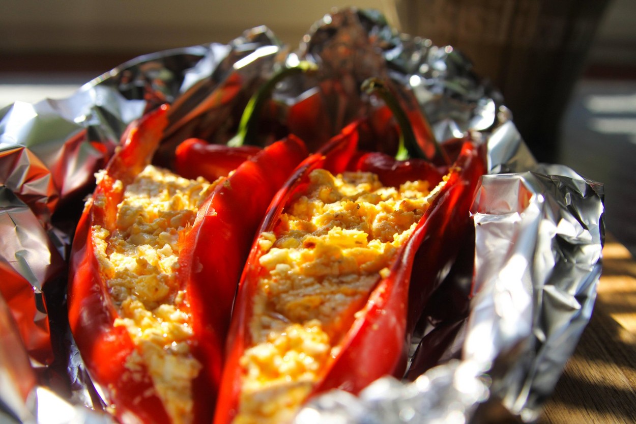 Close up of stuffed red paprika bell peppers with sheep feta cheese seasoned with spicy chili grilled in aluminium foil