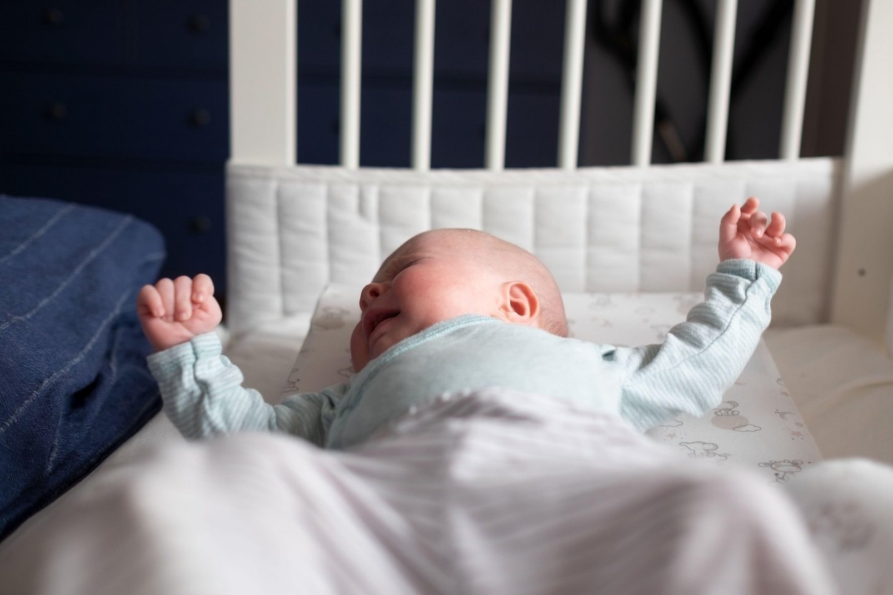 Crying caucasian baby on a bed suffering from colic pain.