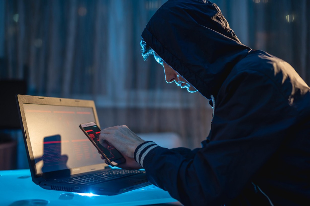 Male hacker in the hood holding the phone in his hands trying to steal access databases with passwords. The concept of cyber security