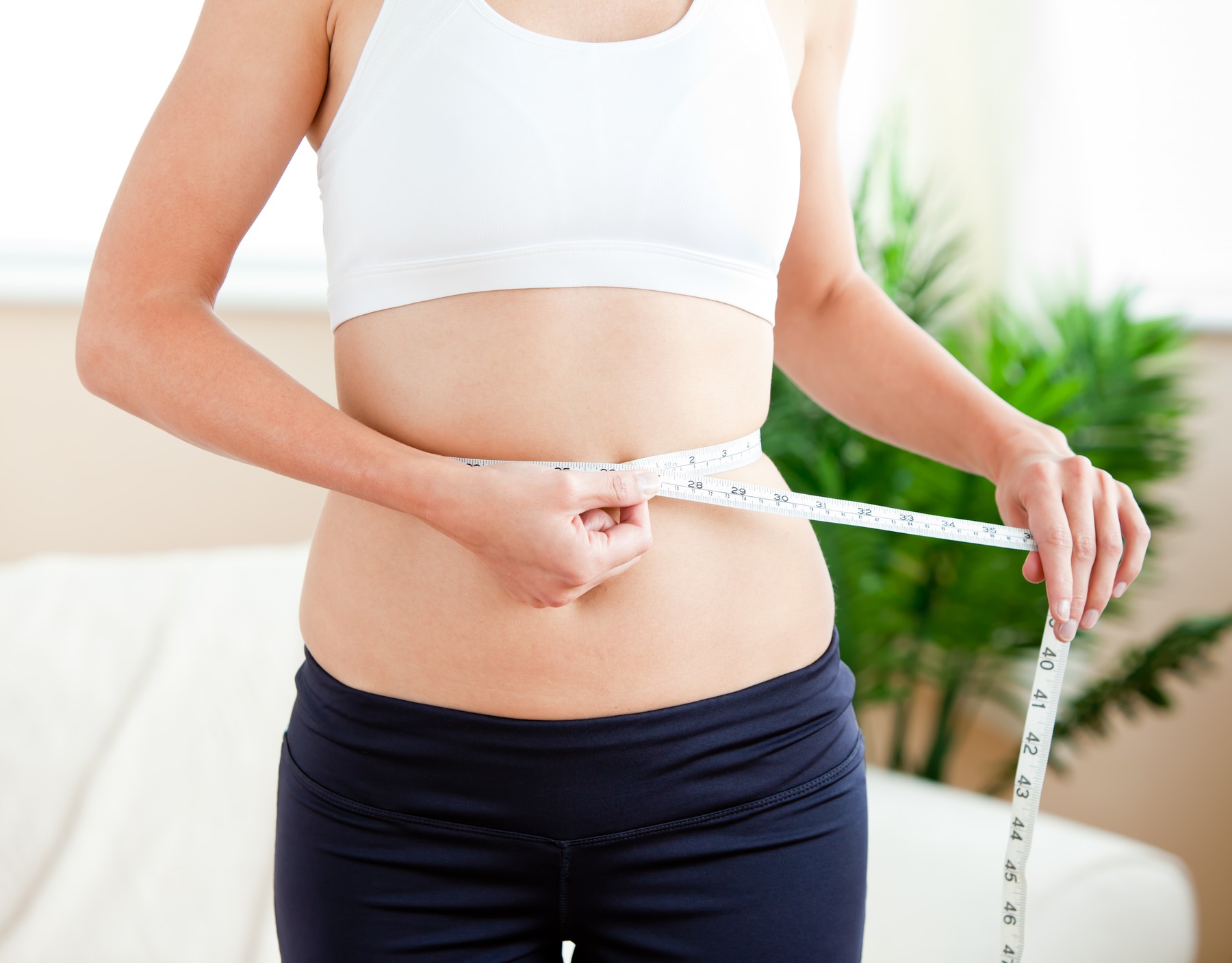 Positive woman measuring her waist with a tape in the living-room