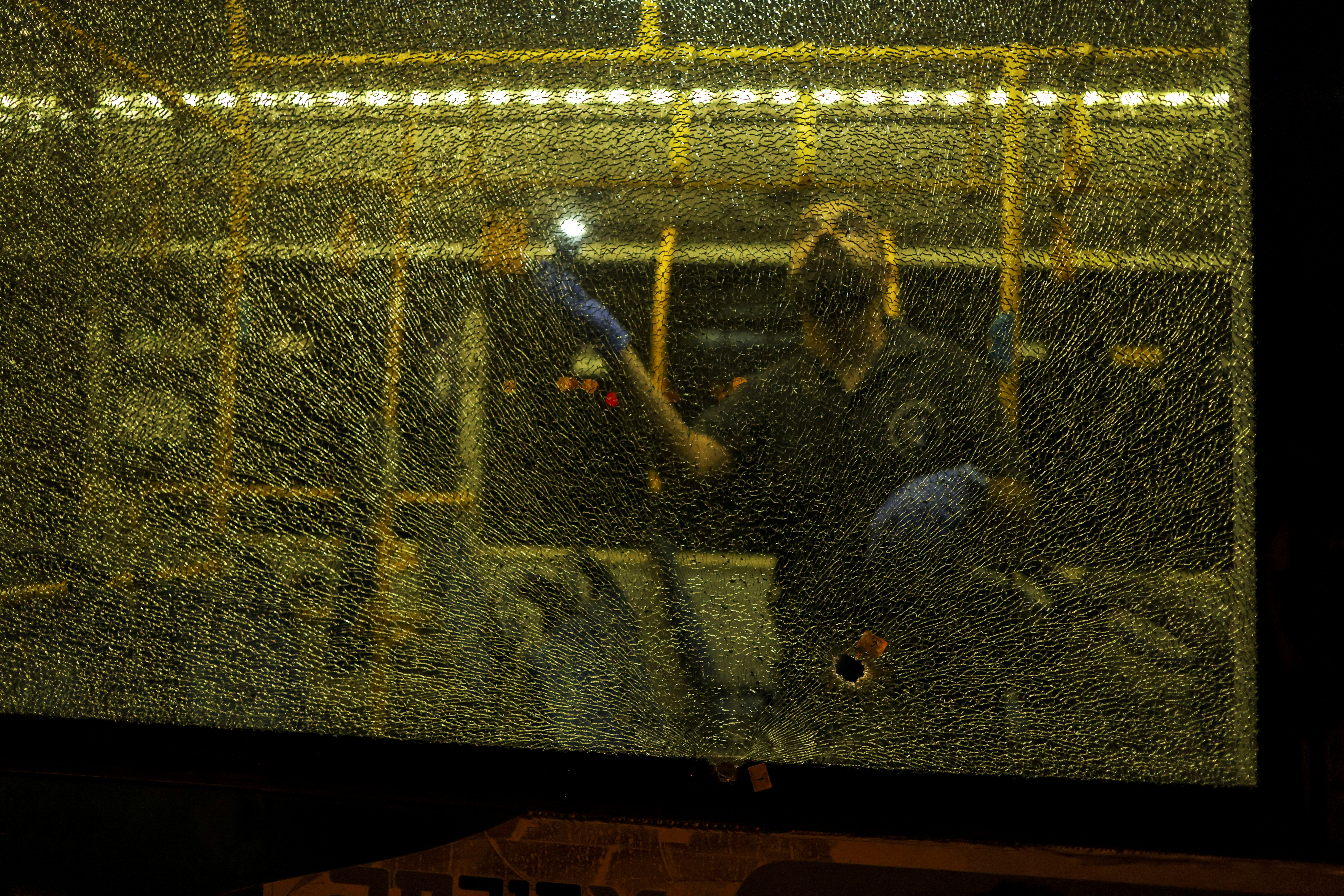 An Israeli security personal stands behind a shattered window of a bus as he checks it following an incident in Jerusalem