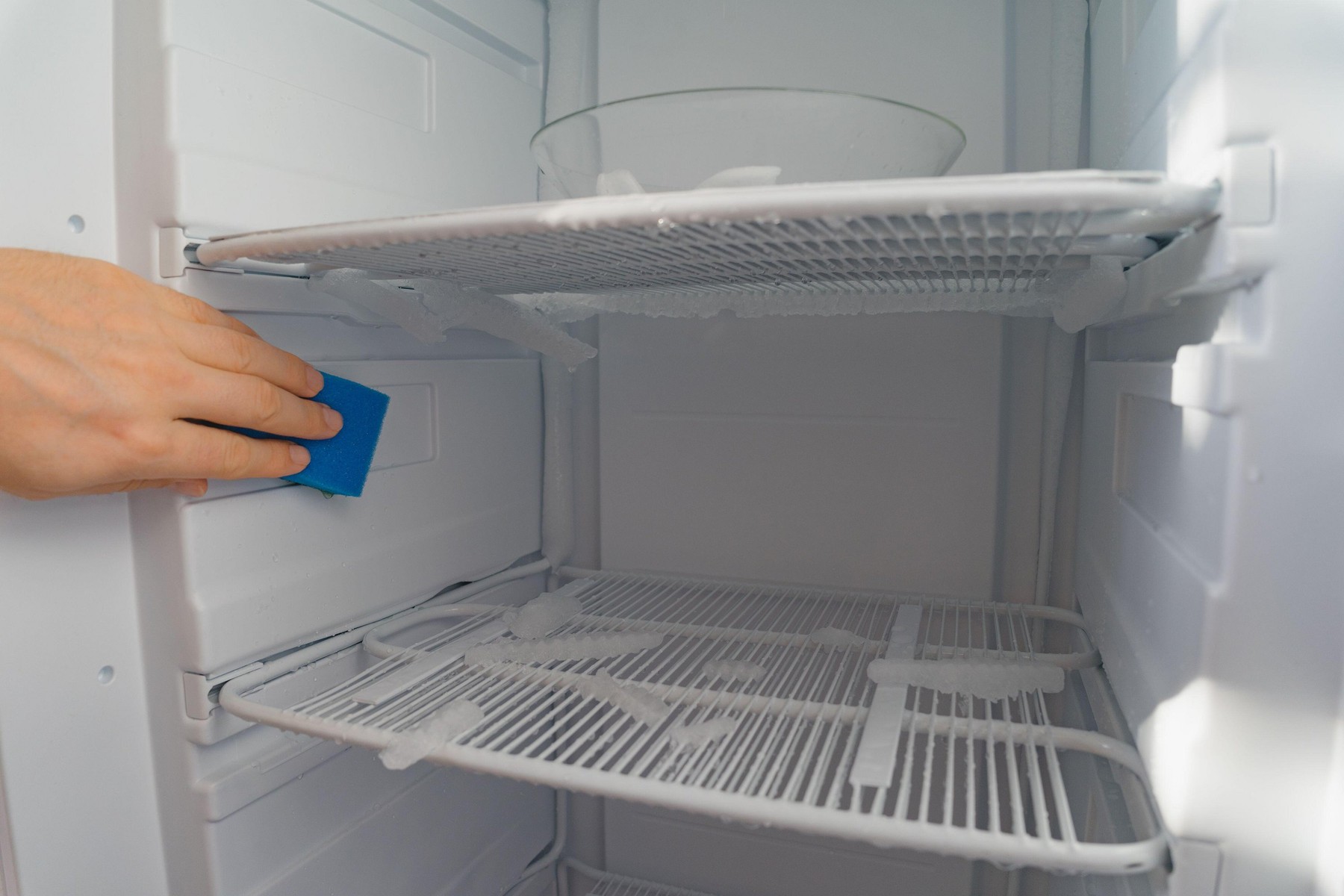 Defrosting and cleaning the freezer. A man wipes meltwater with a sponge. Shallow depth of field. Space for text.