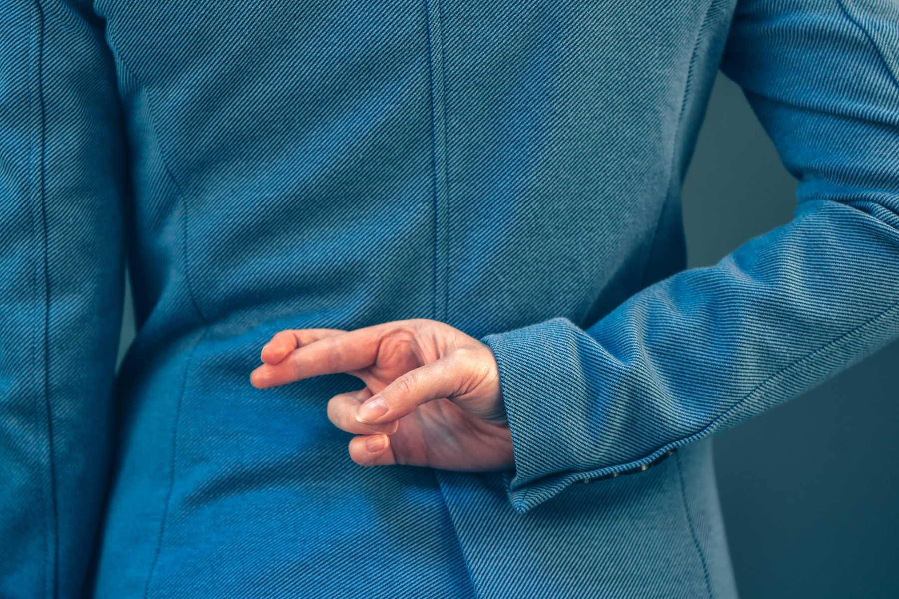 Business woman in elegant blue suit has crossed fingers behind her back as a form of hand gesture when people are telling lies