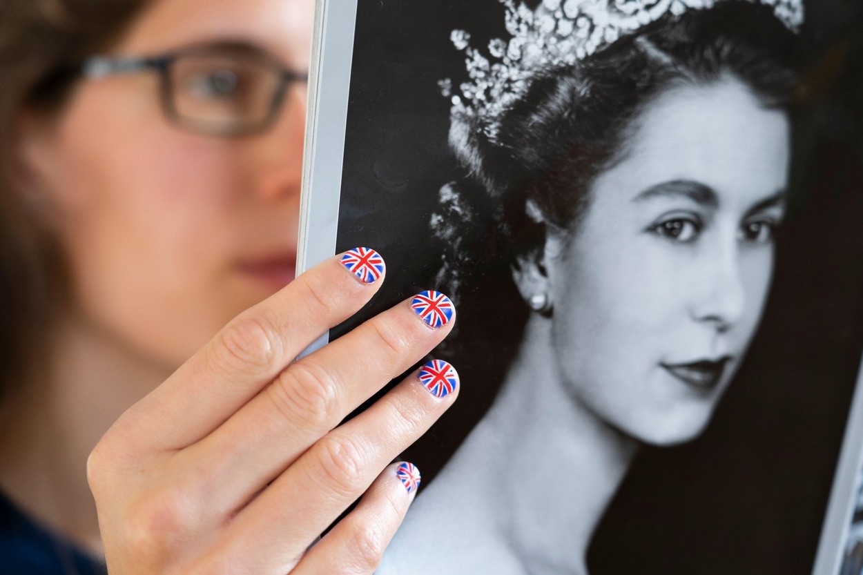 Fan with fingernails painted with the British Flag holding a copy of OK magazine with a portrait of a young Elizabeth II. Platinum Jubilee June 2022