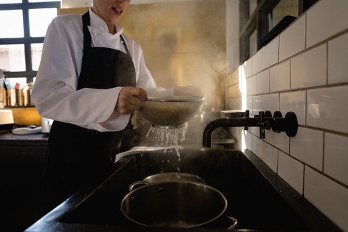 Side view of a Caucasian female chef at a cookery class in a restaurant kitchen, sieving freshly cooked pasta over the sink. Active Seniors enjoying their retirement.