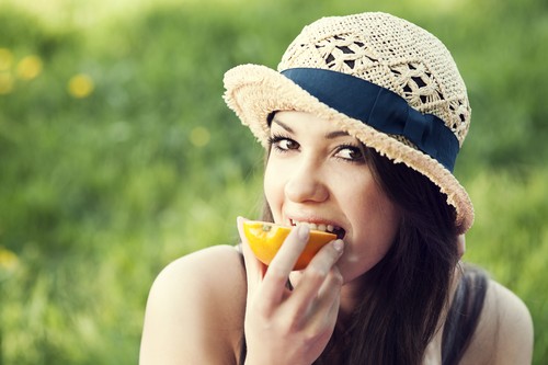 Beautiful woman eating orange on meadow