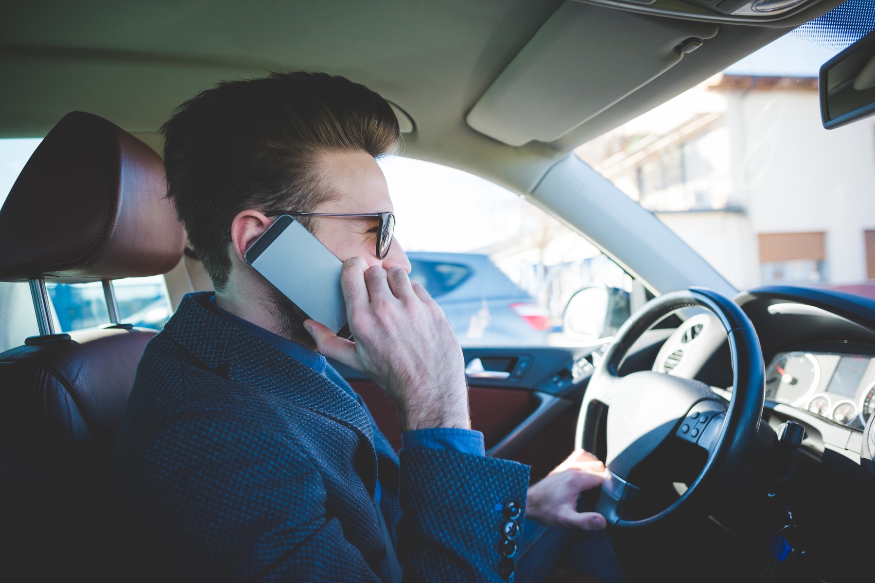 Stylish young man talking on smartphone whilst driving car