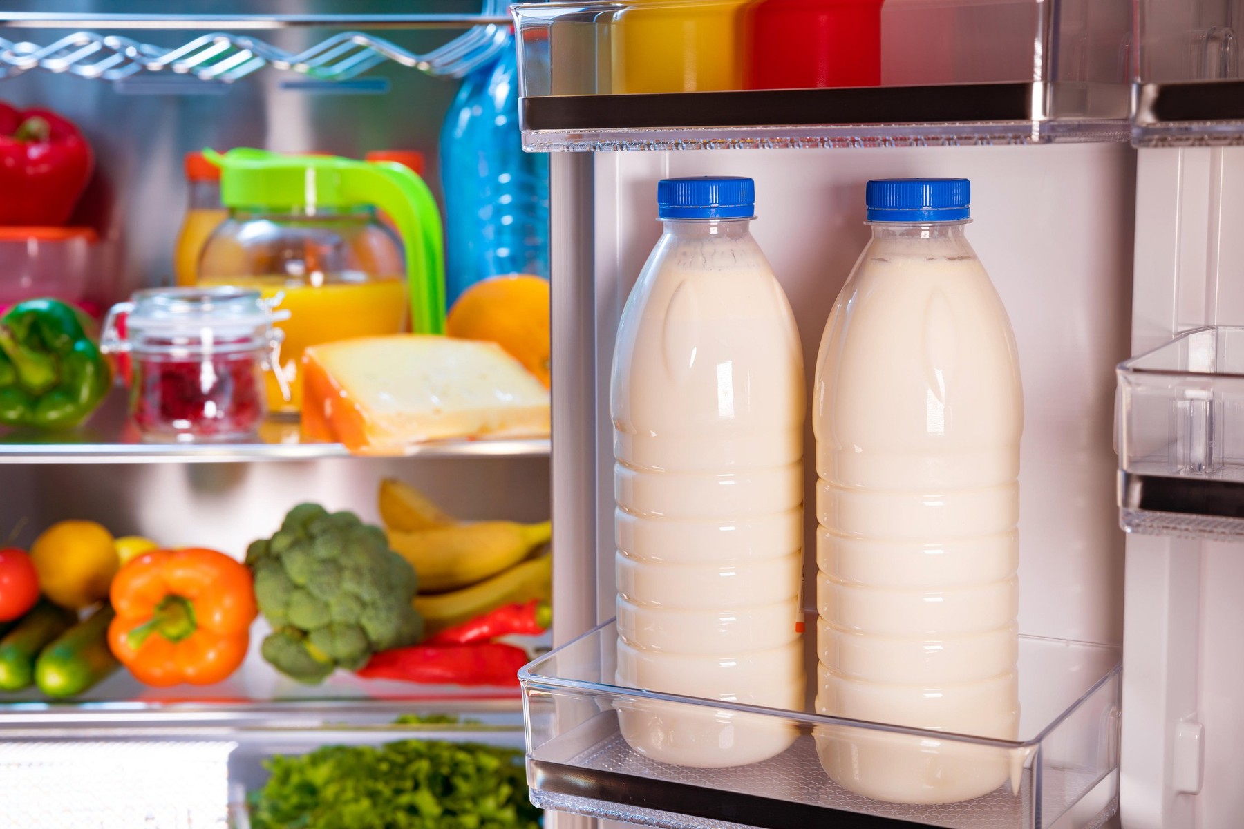 Open refrigerator filled with food. Focus on Bottles of milk in the fridge