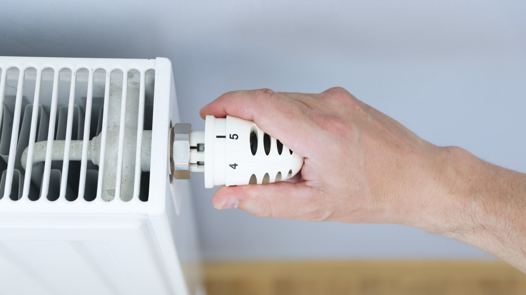 Hand adjusting thermostat valve of heating radiator in a room.