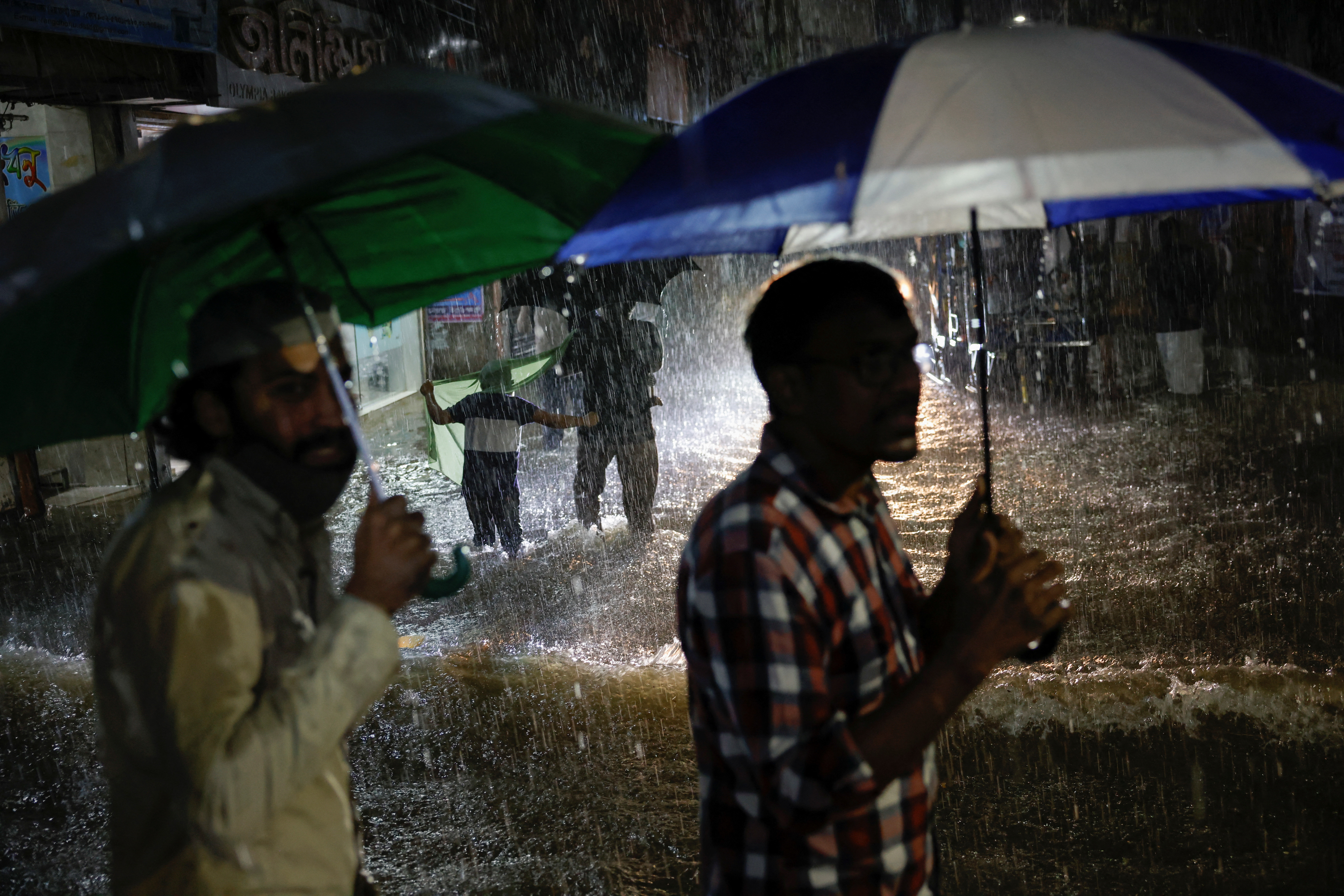 People wade through a flooded street amid continuous rain before the Cyclone Sitrang hits in Dhaka