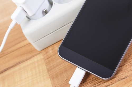 Mobile phone with connected plug of charger, smartphone charging on table