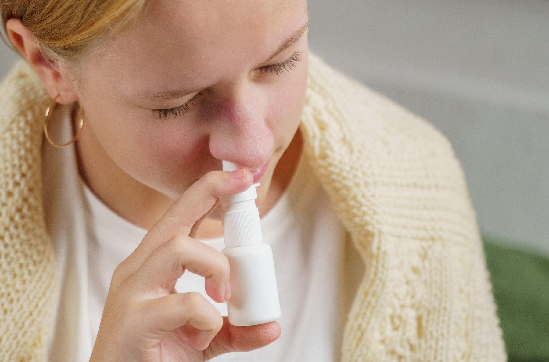 A girl with a cold treats a runny nose with a nasal spray. Medicine and health concept.