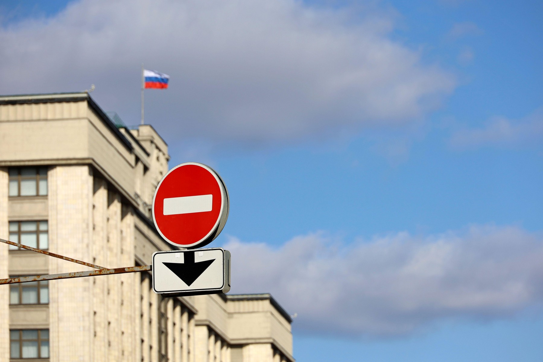 Stop sign on background of State Duma of Russia and Russian flag against blue sky. Concept of economic sanctions due to special military operation