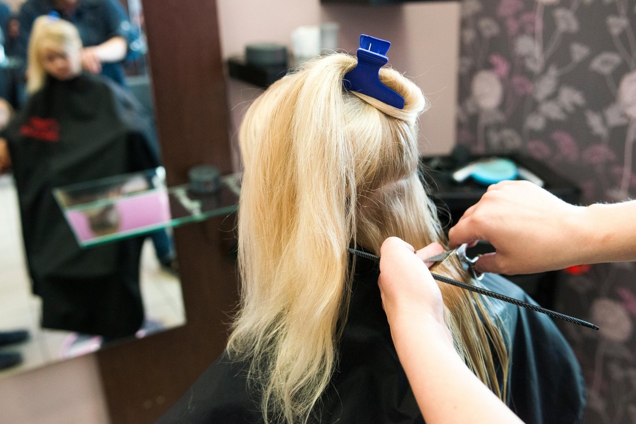 Female hairdresser cutting and brushing young child blond girl hair in hairdressing salon